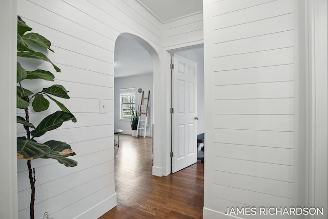 corridor with arched walkways, wood walls, and dark wood-style floors