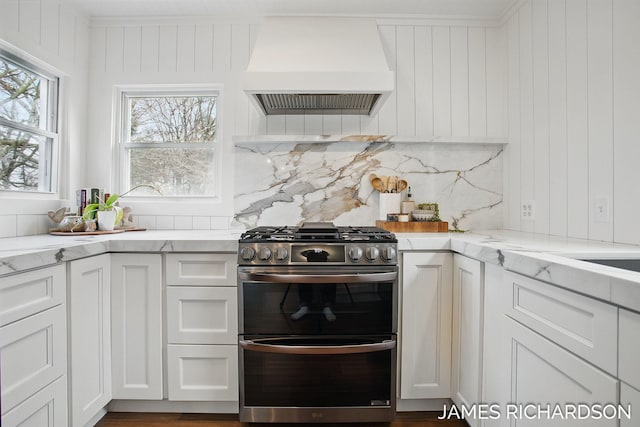 kitchen with tasteful backsplash, light stone counters, double oven range, premium range hood, and white cabinetry
