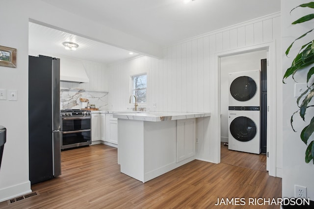 kitchen featuring stacked washer and clothes dryer, wood finished floors, visible vents, premium range hood, and appliances with stainless steel finishes