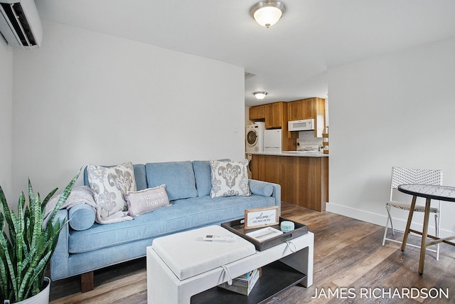 living room with washing machine and dryer, an AC wall unit, baseboards, and wood finished floors