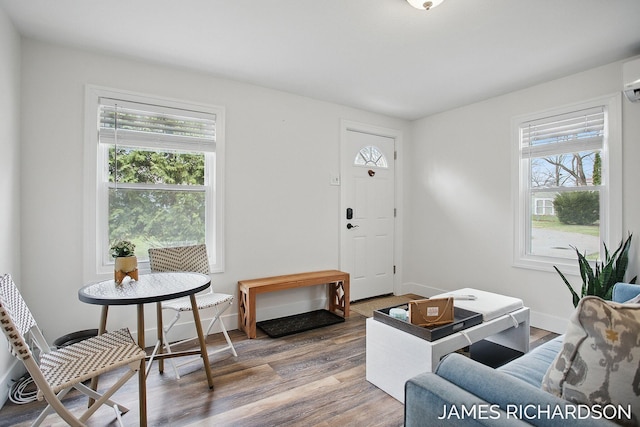 living area featuring an AC wall unit, baseboards, and wood finished floors