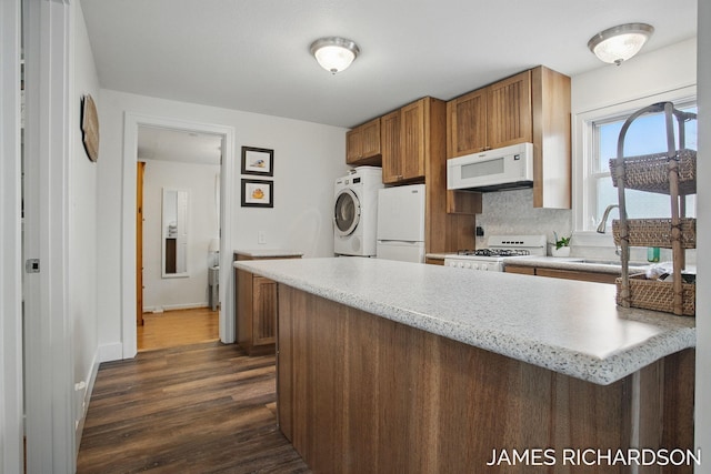 kitchen featuring a peninsula, a sink, dark wood finished floors, white appliances, and washer / dryer