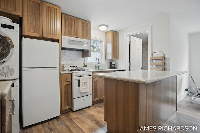kitchen with a sink, brown cabinets, stacked washing maching and dryer, white appliances, and dark wood-type flooring
