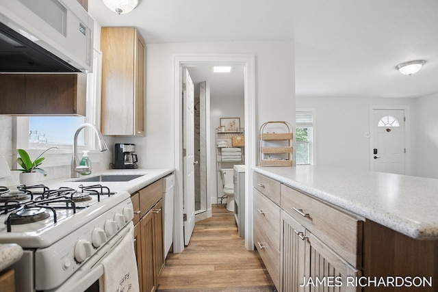 kitchen with light wood finished floors, a sink, white appliances, and exhaust hood