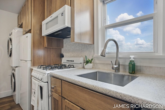 kitchen featuring brown cabinets, stacked washer / dryer, a sink, and white appliances