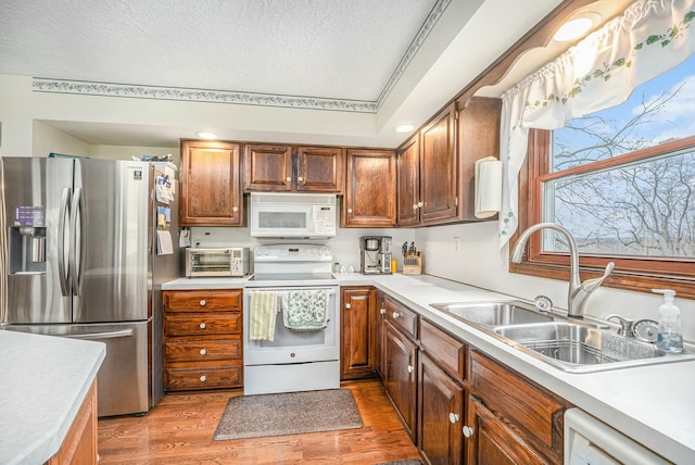 kitchen with white appliances, a sink, light countertops, light wood finished floors, and brown cabinetry