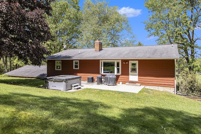 back of house with a hot tub, a chimney, a patio area, and a lawn