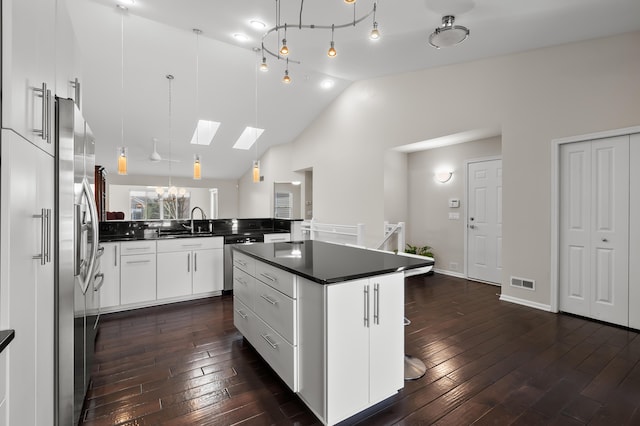 kitchen with vaulted ceiling with skylight, dark countertops, stainless steel appliances, and dark wood-style floors