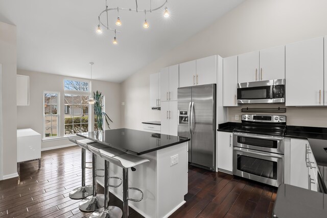 kitchen featuring lofted ceiling, dark countertops, dark wood-style floors, white cabinetry, and stainless steel appliances