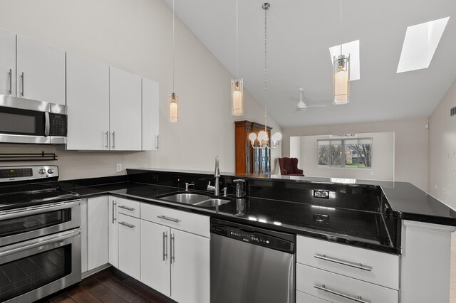 kitchen featuring dark countertops, lofted ceiling with skylight, a sink, dark wood finished floors, and stainless steel appliances