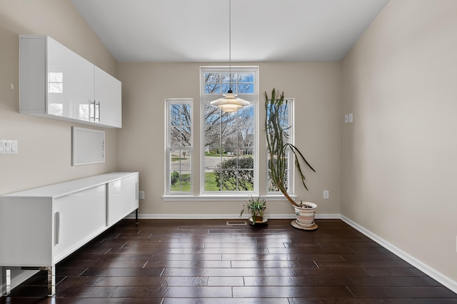 unfurnished dining area featuring baseboards, dark wood-style flooring, and a wealth of natural light