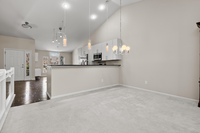 kitchen featuring dark countertops, baseboards, high vaulted ceiling, stainless steel microwave, and a chandelier