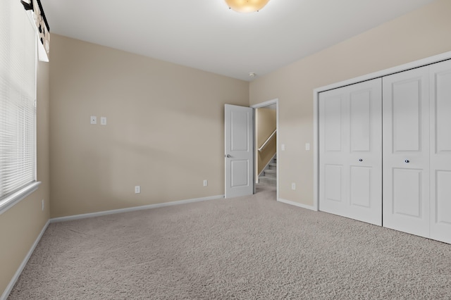 unfurnished bedroom featuring carpet floors, multiple windows, baseboards, and a closet