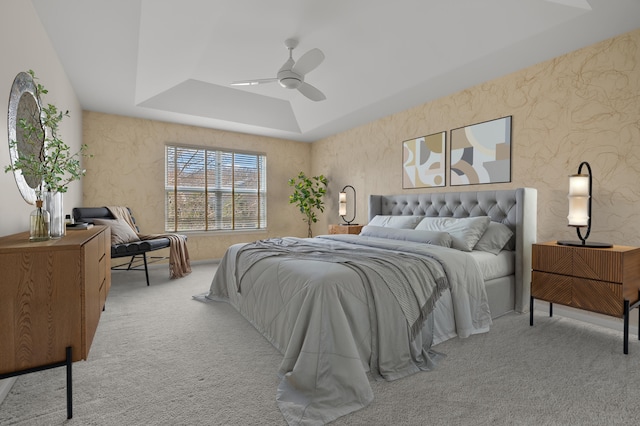 carpeted bedroom featuring a raised ceiling and a ceiling fan