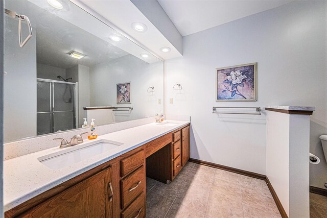 bathroom with a stall shower, double vanity, baseboards, and a sink