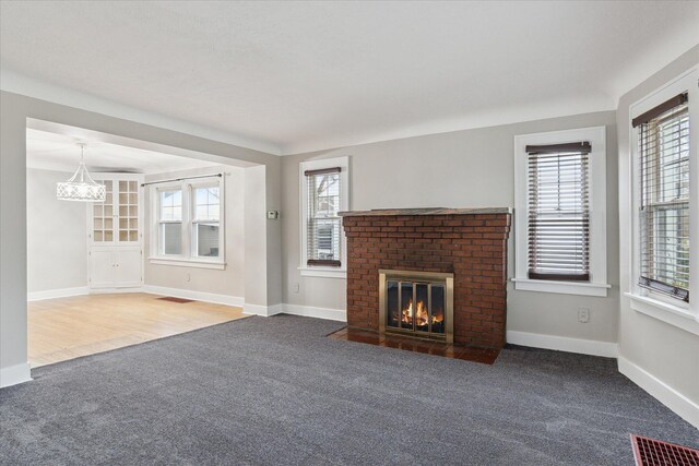 unfurnished living room featuring a brick fireplace, carpet, baseboards, and visible vents