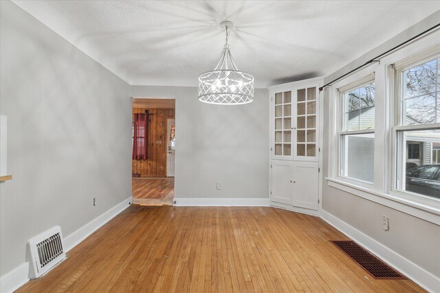 unfurnished dining area with light wood-type flooring, an inviting chandelier, baseboards, and visible vents