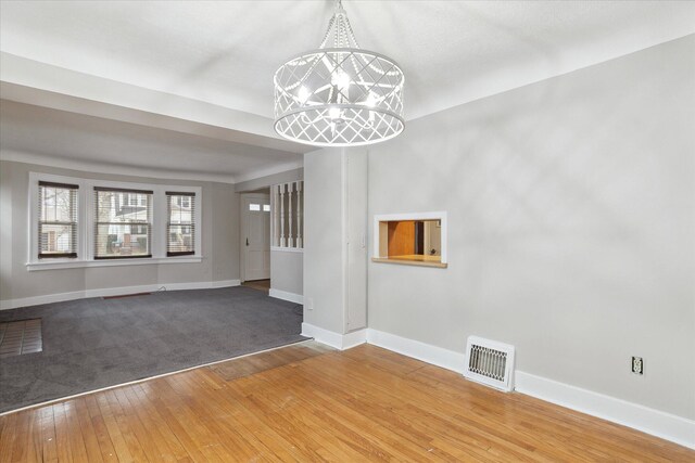 unfurnished living room featuring wood-type flooring, baseboards, visible vents, and an inviting chandelier