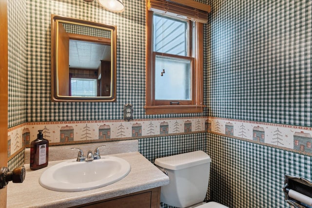 half bathroom featuring wallpapered walls, vanity, a wainscoted wall, and toilet