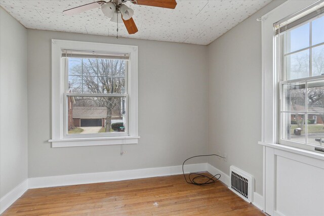 unfurnished room featuring a ceiling fan, a healthy amount of sunlight, light wood finished floors, and visible vents