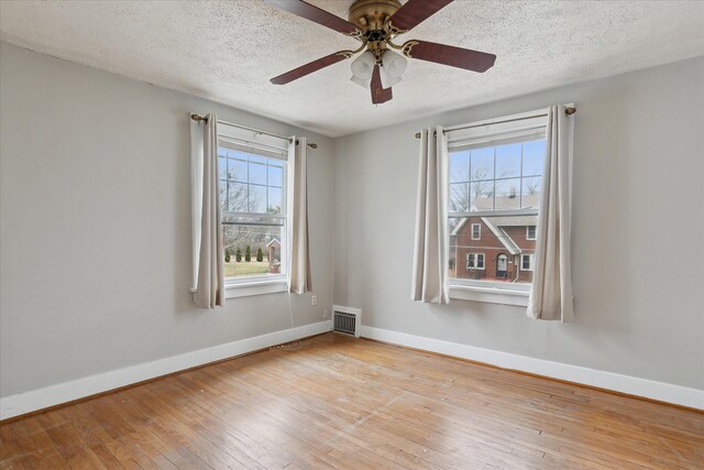 empty room featuring plenty of natural light, baseboards, visible vents, and hardwood / wood-style floors