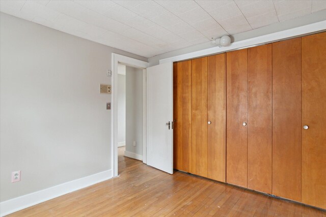 unfurnished bedroom featuring baseboards, light wood-type flooring, and a closet