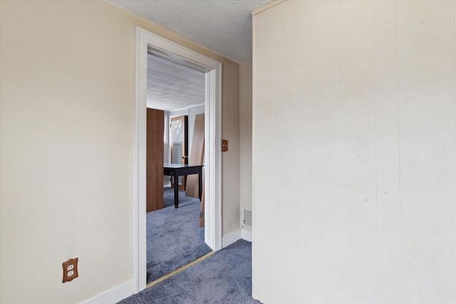 corridor featuring baseboards, carpet floors, and a textured ceiling