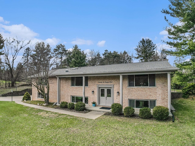 raised ranch featuring french doors, a shingled roof, a front yard, and brick siding
