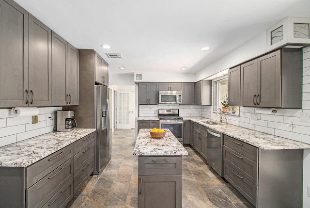 kitchen featuring stainless steel appliances, stone finish floor, a sink, and decorative backsplash