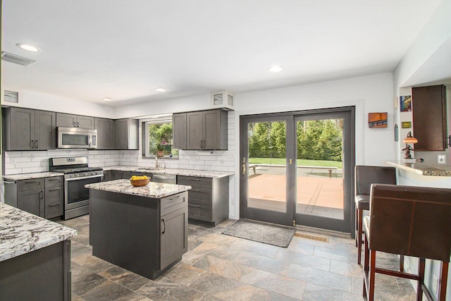 kitchen with visible vents, light stone countertops, backsplash, a kitchen island, and stainless steel appliances