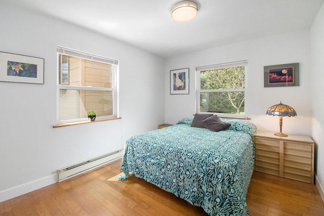bedroom with a baseboard heating unit, baseboards, and wood finished floors
