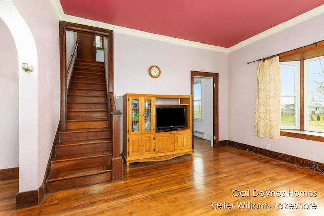staircase featuring crown molding, baseboards, wood finished floors, arched walkways, and a baseboard heating unit