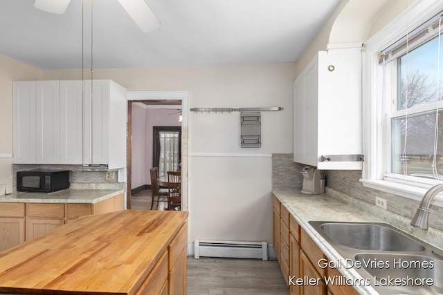 kitchen featuring decorative backsplash, a baseboard radiator, a ceiling fan, a sink, and black microwave