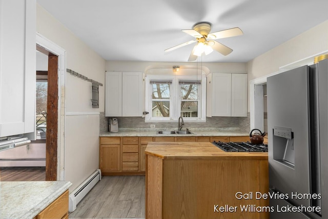 kitchen with stainless steel fridge, butcher block countertops, gas stovetop, a sink, and a baseboard radiator