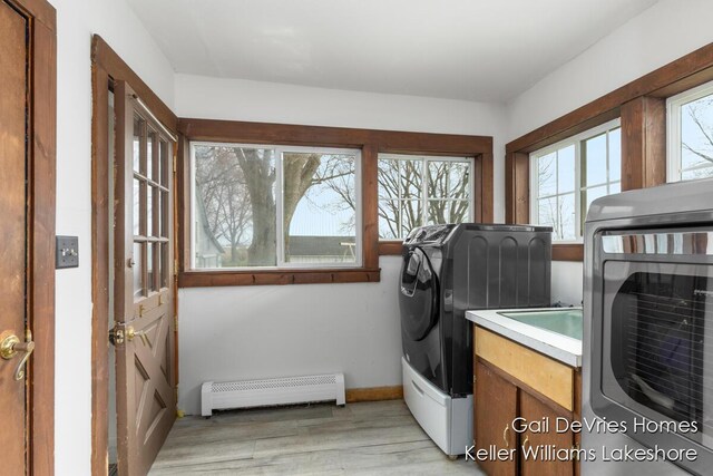 laundry area with baseboards, laundry area, a baseboard heating unit, light wood-style floors, and washer and clothes dryer