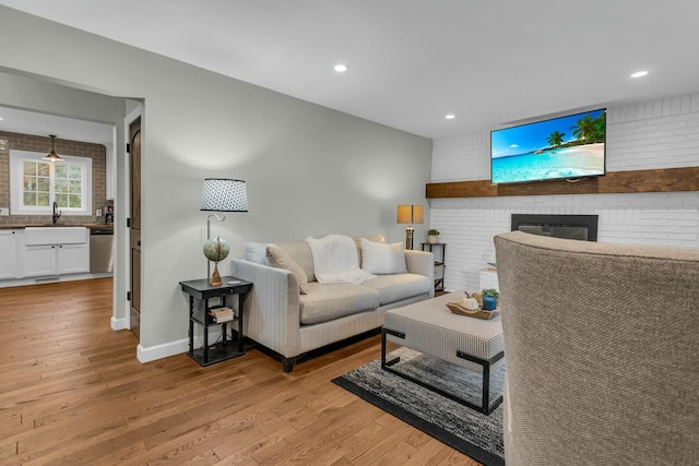 living room with a fireplace, light wood-style floors, and brick wall