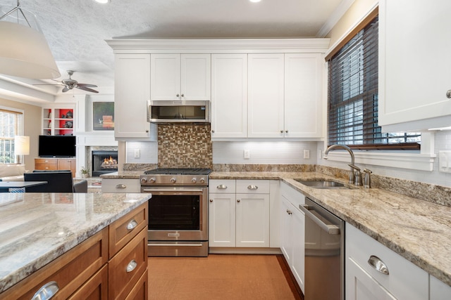 kitchen with a sink, a ceiling fan, white cabinetry, a fireplace, and stainless steel appliances