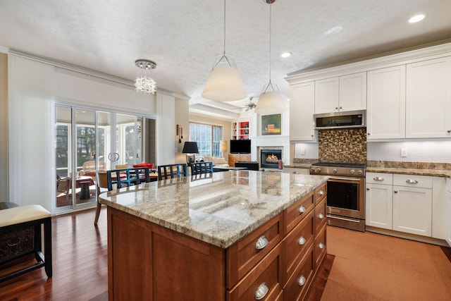 kitchen featuring a warm lit fireplace, white cabinets, stainless steel appliances, light stone counters, and a center island