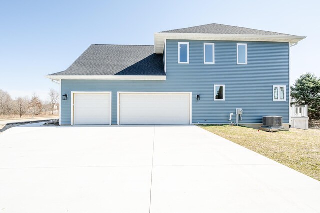 exterior space with a garage, central air condition unit, concrete driveway, a shingled roof, and a front yard
