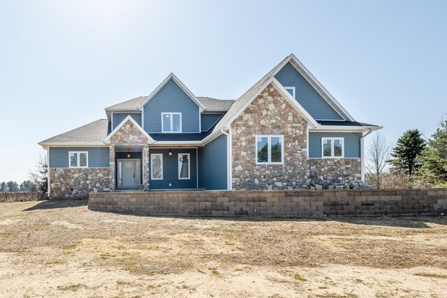 craftsman-style house with stone siding, a porch, and roof with shingles