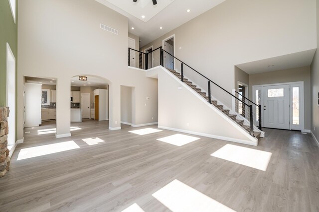 unfurnished living room featuring arched walkways, a high ceiling, stairs, and baseboards