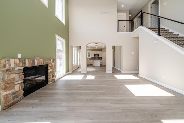 unfurnished living room featuring baseboards, a healthy amount of sunlight, a high ceiling, and a fireplace