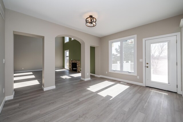 unfurnished dining area featuring baseboards, wood finished floors, a stone fireplace, and arched walkways