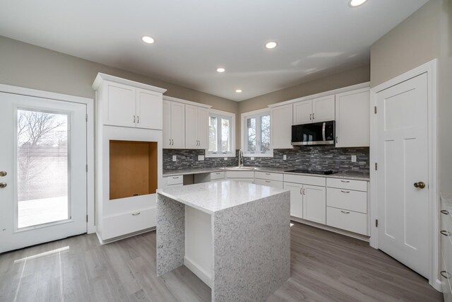kitchen with backsplash, a sink, stainless steel microwave, a center island, and black electric stovetop