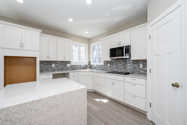 kitchen with white cabinets, a sink, stainless steel microwave, light wood-style floors, and backsplash