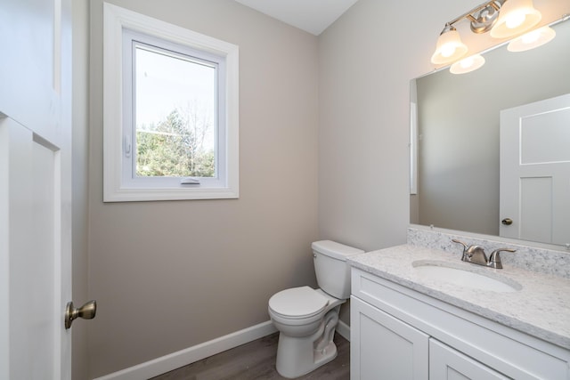 half bath featuring toilet, vanity, wood finished floors, and baseboards