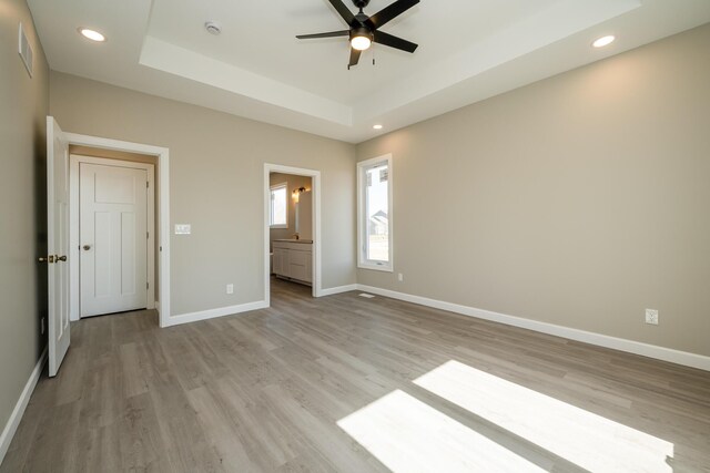 unfurnished bedroom featuring baseboards, light wood-style floors, and a raised ceiling