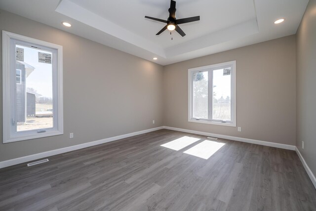 empty room featuring a tray ceiling, baseboards, visible vents, a ceiling fan, and wood finished floors
