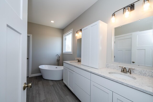 full bath featuring a freestanding bath, wood finished floors, a sink, and double vanity