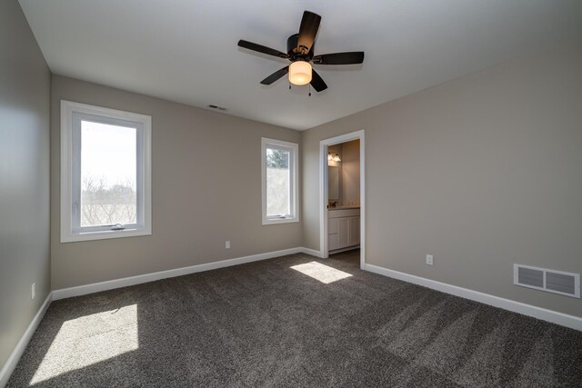 spare room with dark colored carpet, visible vents, and plenty of natural light